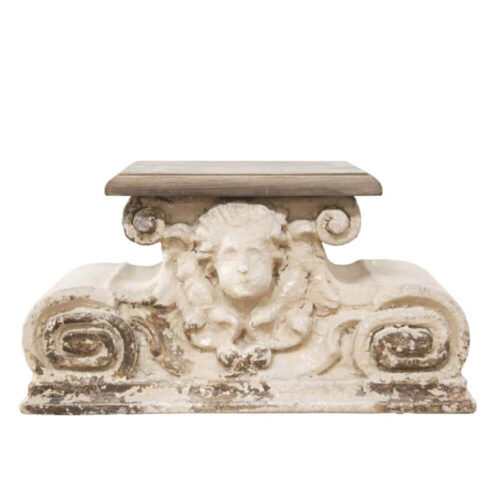 Base decorativa a forma di capitello con dettagli classici e volto d’angelo, in resina effetto anticato bianco-beige.