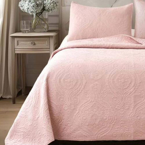 Trapunta rosa cipria con elegante motivo ricamato e federa abbinata su letto matrimoniale, stile shabby chic.