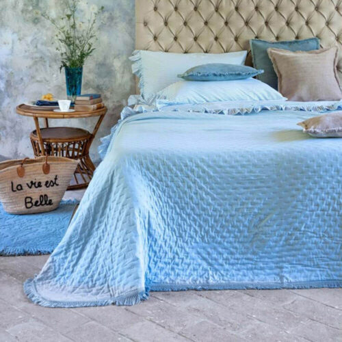 Trapunta matrimoniale azzurra con texture trapuntata e bordo sfrangiato, stesa su letto in stile shabby chic.