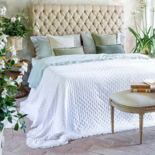 Double édredon blanc avec texture matelassée et bordure frangée, sur un lit élégant dans un décor printanier.