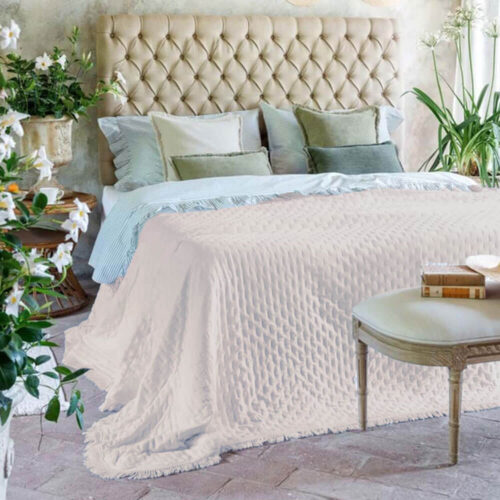 Trapunta matrimoniale color naturale con texture trapuntata e frange, stesa su letto in stile romantico e floreale.