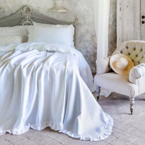 Colcha doble blanca "Blanc MariClo" con volante fruncido y tela de lunares pequeños sobre una cama Shabby Chic, con dos fundas de almohada a juego.
