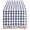 Runner Blanc Mariclò a quadri blu e bianchi con bordo floreale arricciato, su tavolo rustico con dolci e frutta.