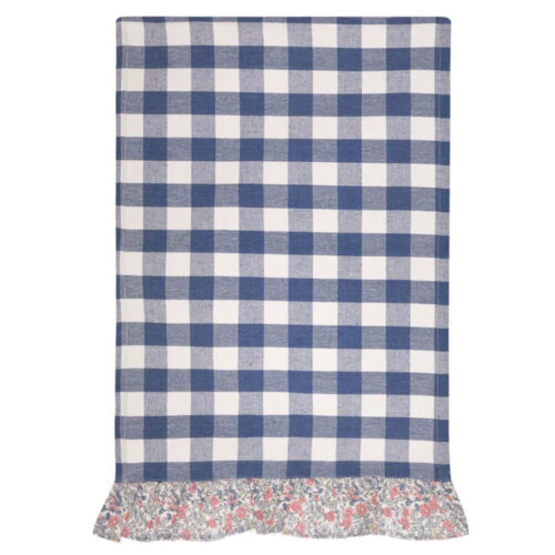 Canovaccio Blanc Mariclò con fantasia vichy blu e bordo floreale arricciato, steso su tavolo rustico.