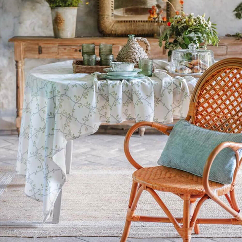 Blanc MariClò Nappe Rami d'Amore 140x180 cm 1 Nappe rectangulaire Blanc MariClò avec un motif vert de branches entrelacées sur fond crème, dans une ambiance rustique.