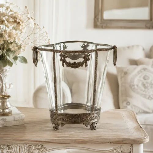 Vaso decorativo in vetro trasparente con struttura in ottone brunito, manici laterali ad anello e fregi floreali in rilievo.