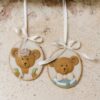 Medallón colgante ovalado Sweet Bear con oso en relieve, lazo marfil y borde dorado, variantes surtidas.