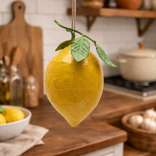 Adorno colgante de limón de metal amarillo con dos hojas verdes en relieve y cordón de fibra natural.