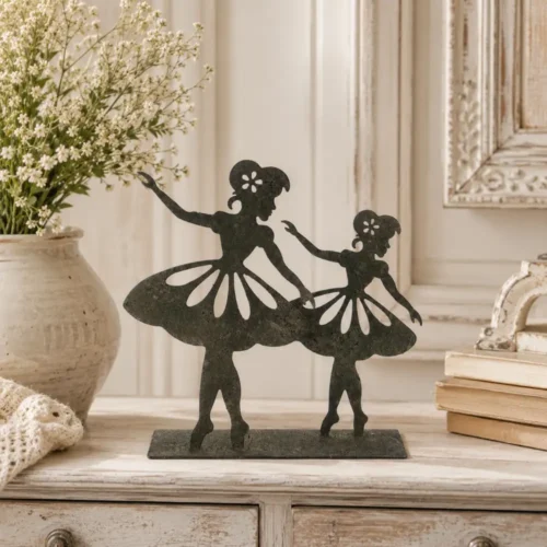 Decorazione in ferro con due ballerine stilizzate su base piatta, finitura effetto anticato, esposta su mobile in legno con piante.