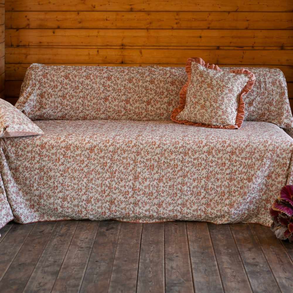 Colcha de algodón Jaipur con estampado floral rosa y detalles de terciopelo, drapeada sobre sofá de madera.