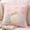 Cuscino rosa cipria con applicazioni a uova pastello, coniglietto stilizzato con fiocco beige e pom pon decorativi.