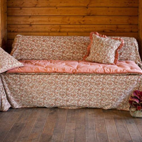 Dessus de canapé Jaipur en velours rose saumoné matelassé avec bord incurvé, placé sur le canapé avec housse florale assortie.