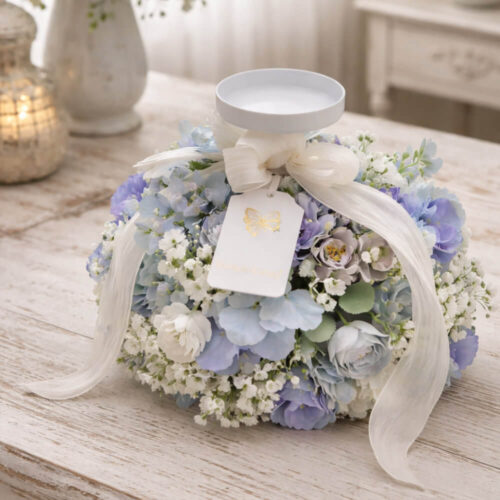 Candelabro Fiori di Lena con ortensia azzurro polvere e nebbiolina bianca, fiocco avorio e piattino portacandela, su tavolo in legno shabby chic.