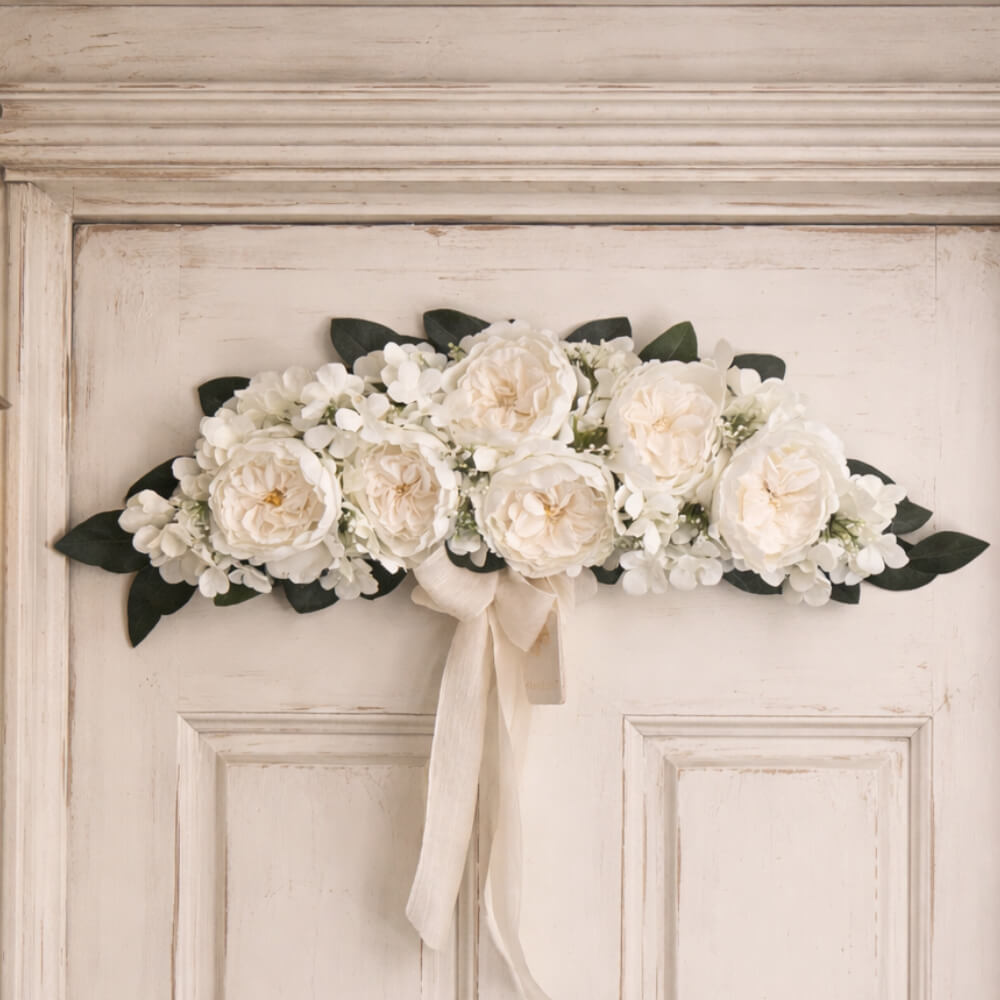 Colgante de pared floral Fiori di Lena con 6 peonías blancas, hortensias y muérdago, lazo claro y vegetación decorativa.