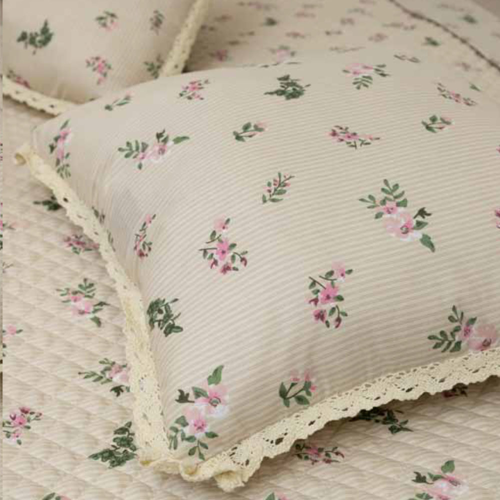 Cojín decorativo cuadrado Flor de Primavera L'Atelier 17 de poliéster rayado marfil con estampado floral rosa y amplio borde de encaje de ganchillo, colocado sobre colcha a juego.