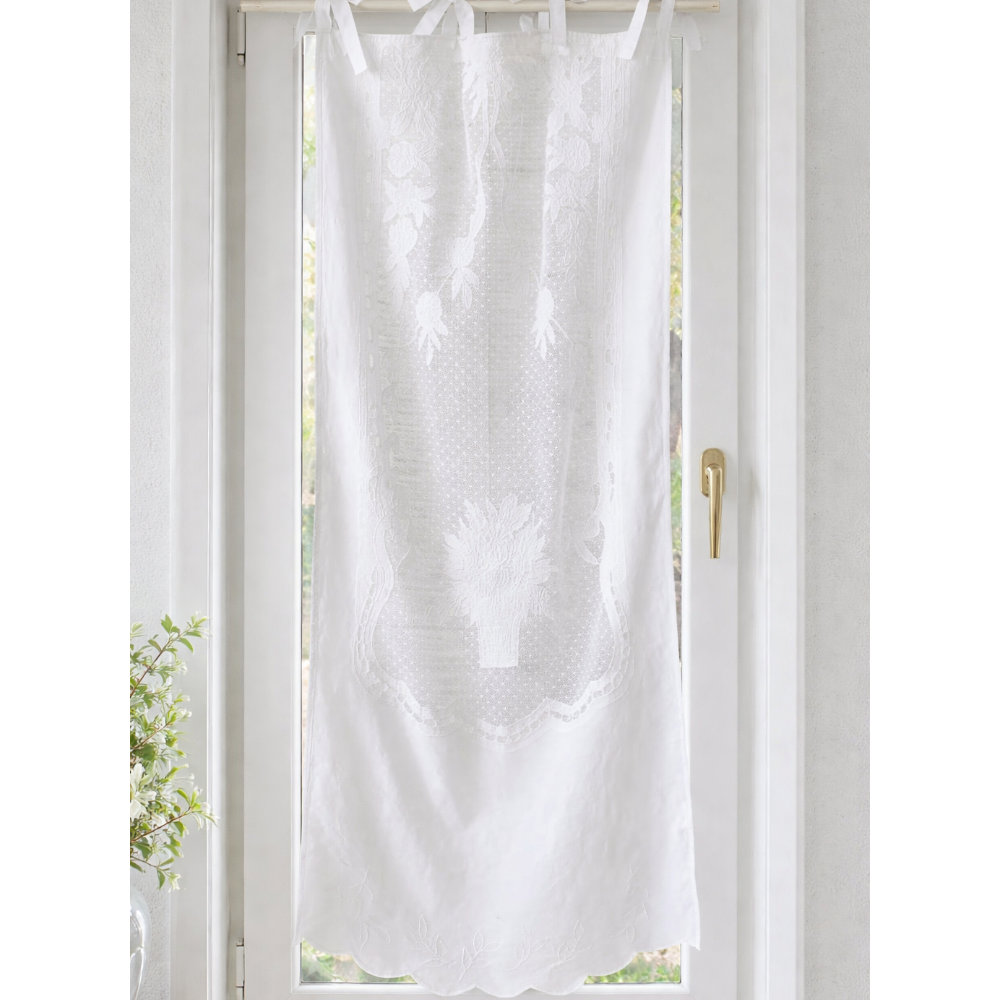 Tendina Provenzale Margareth L'Atelier 17 in cotone bianco con ricami floreali tridimensionali su pizzo puntinato, medaglione centrale a vaso fiorito e bordo inferiore a festoni sagomati, fissaggio a passanti con fiocchi in raso.