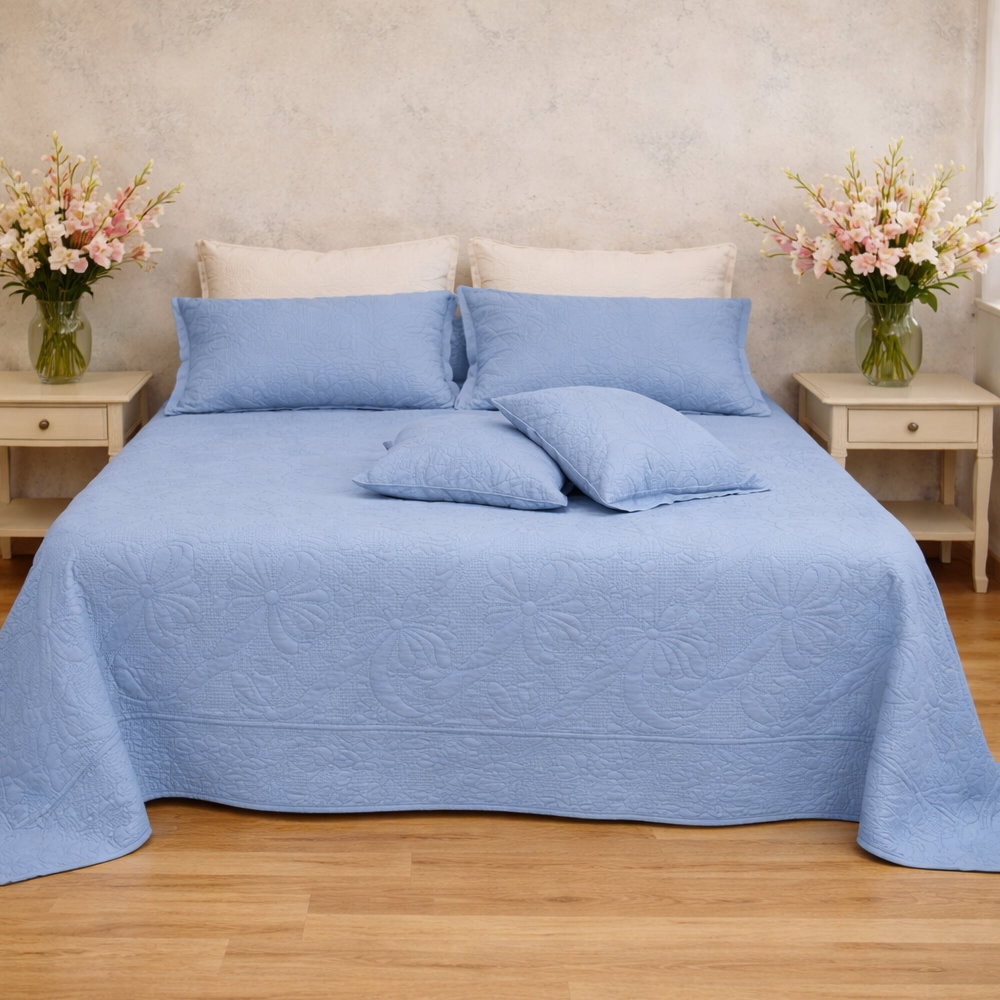 Colcha doble L'Atelier 17 de poliéster azul cielo con acolchado de nido de abeja y motivo en relieve tono sobre tono de lazos y volutas, borde en forma de festón, con fundas de almohada a juego en cama doble.