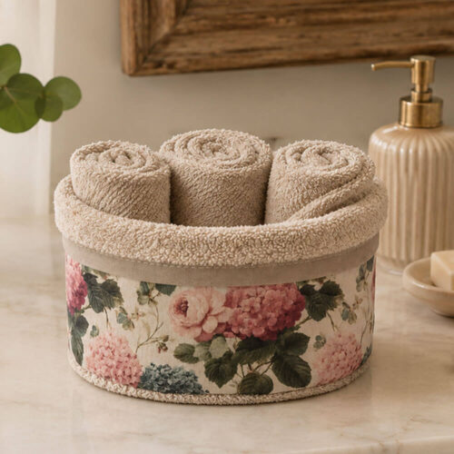 Cestino contenitore in cotone beige con tre lavette arrotolate e fascia decorativa floreale con ortensie e rose nei toni rosa, verde e crema.
