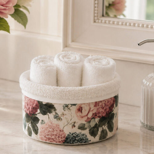 Cestino rivestito con stampa floreale rosa e ortensie, completo di tre lavette bianche arrotolate in cotone, ideale per bagno shabby chic.