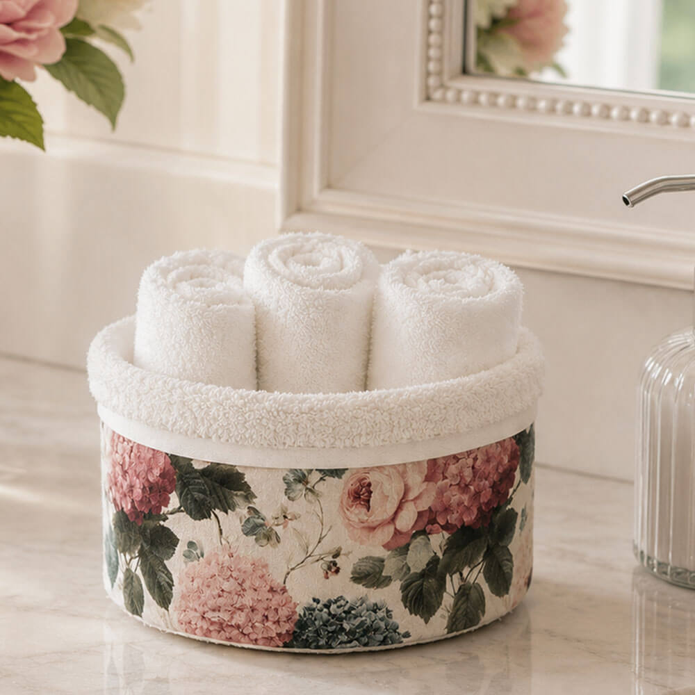 Cestino rivestito con stampa floreale rosa e ortensie, completo di tre lavette bianche arrotolate in cotone, ideale per bagno shabby chic.