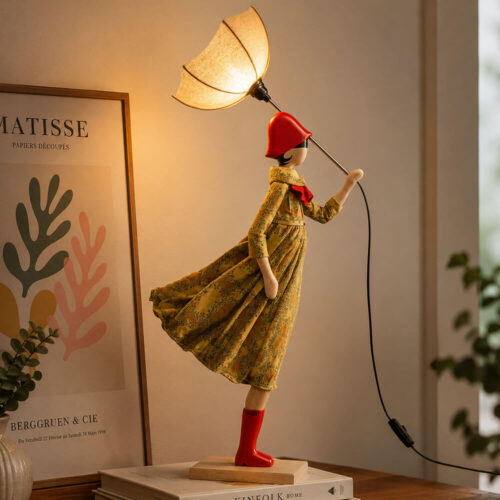 Lampada artigianale SKITSO Little Girl Ismeria con base in legno di faggio, abito floreale beige e verde, dettagli rossi e paralume nocciola a forma di ombrello.