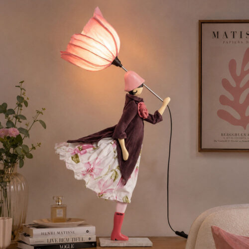 Lampada artigianale SKITSO Little Girl Stimona alta 85 cm, con paralume rosa a forma di fiore, cappotto color prugna e gonna floreale rosa e bianca.