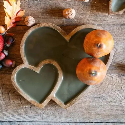 Svuotatasche a forma di doppio cuore in legno di mango con interno smaltato verde salvia, utilizzato come centrotavola su un tavolo in legno con decorazioni autunnali.