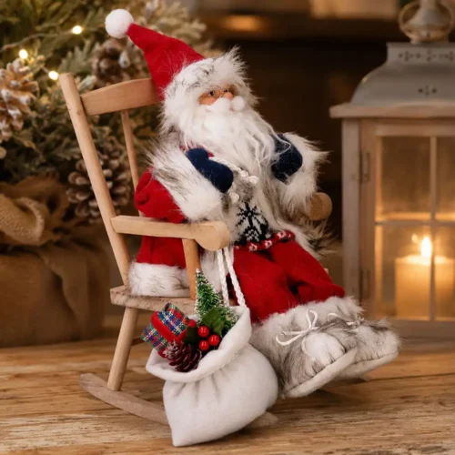Babbo Natale decorativo con lunga barba bianca, abito rosso e finiture in ecopelliccia, seduto su una sedia a dondolo in legno con sacco dono bianco decorato.