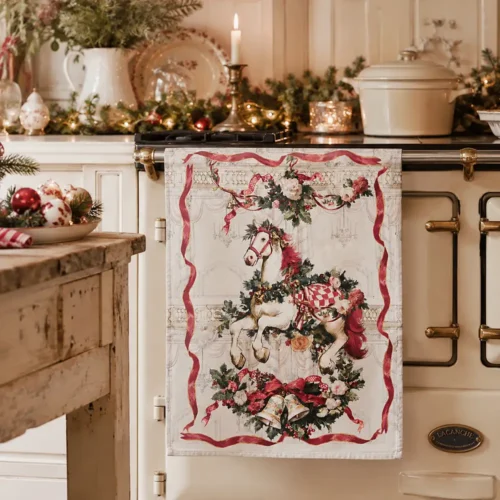 Torchon de Noël en coton « Blanc MariClò » représentant un petit cheval à bascule orné de guirlandes, de fleurs, de rubans rouges et de clochettes, issu de la collection « Calessi e Calessini ».