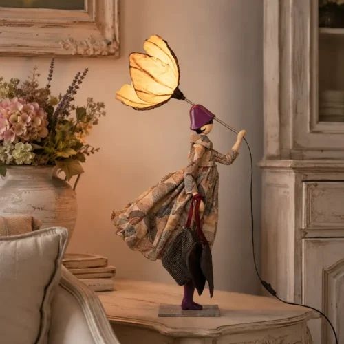 Lampada da tavolo Filyra SKITSO della collezione Little Girls, con abito in tessuto geometrico, dettagli viola, borse decorative e paralume floreale.