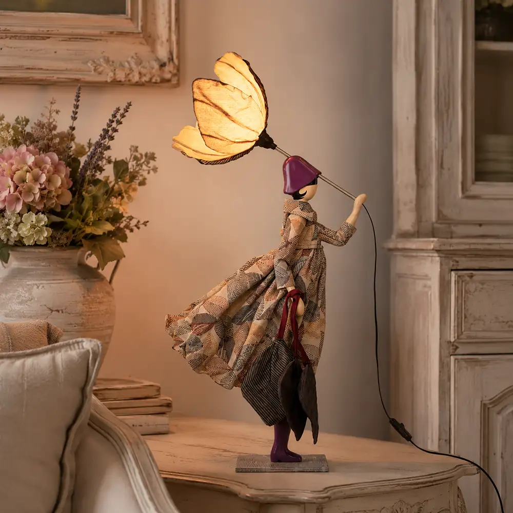Lampada da tavolo Filyra SKITSO della collezione Little Girls, con abito in tessuto geometrico, dettagli viola, borse decorative e paralume floreale.