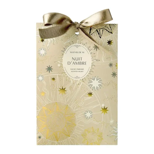 Bolsita perfumada Mathilde M Nuit d'ambre de color marfil, con motivos celestes dorados, una etiqueta ovalada en el centro y un lazo satinado en dorado antiguo.