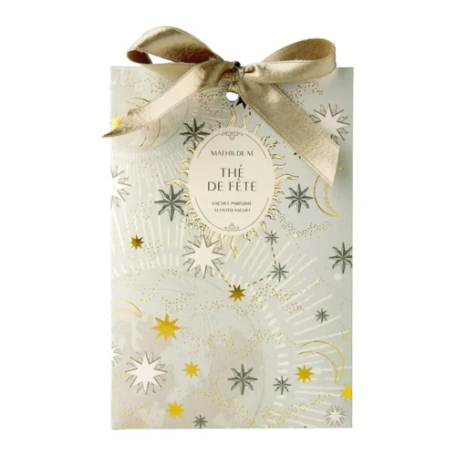 Sachet profumato Mathilde M Thé de Fête color avorio, decorato con stelle e lune dorate, etichetta ovale centrale e fiocco oro champagne.