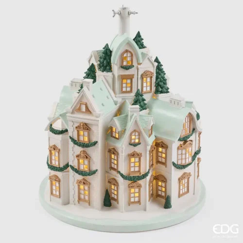 Base per albero EDG a forma di palazzi bianchi e verde acqua, con finestre dorate illuminate, abeti e ghirlande verdi.