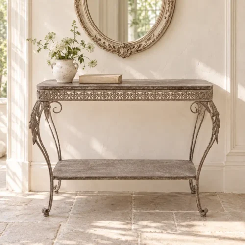 Consola «Blanc MariClò» de Mariclò Antica Officina, de metal envejecido, con friso calado, patas en forma de volutas y estante inferior.